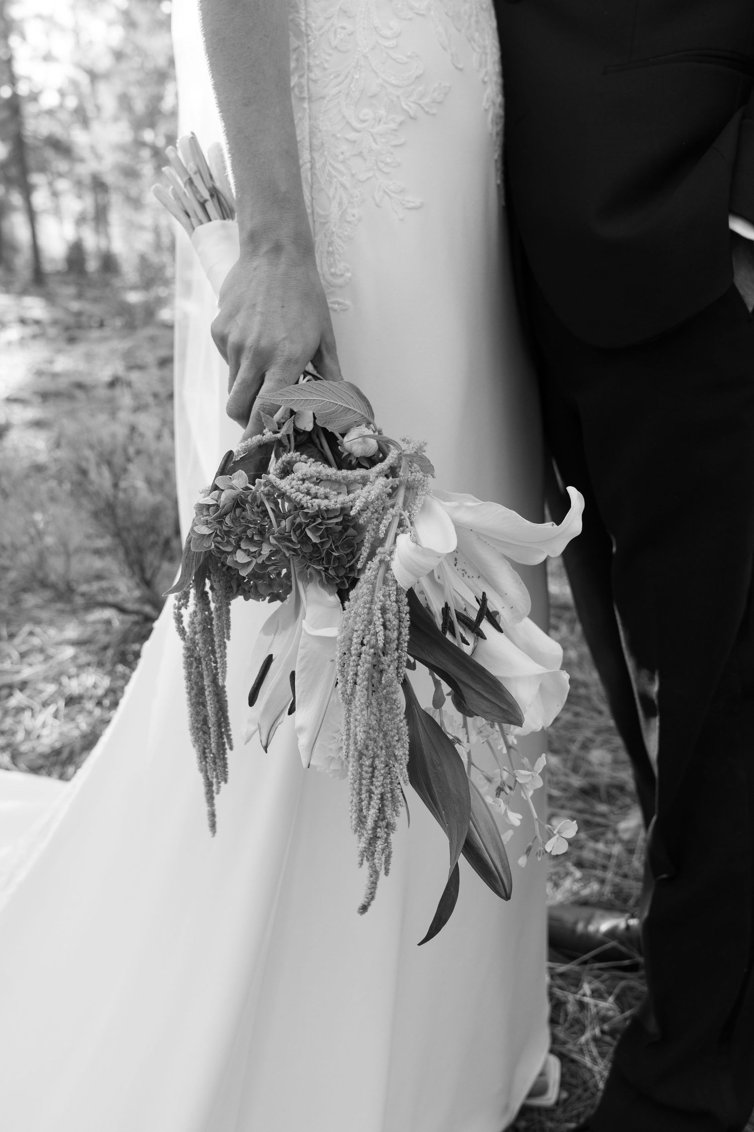 Black and white detail shot of a wedding bouquet with trailing elements against a white dress.