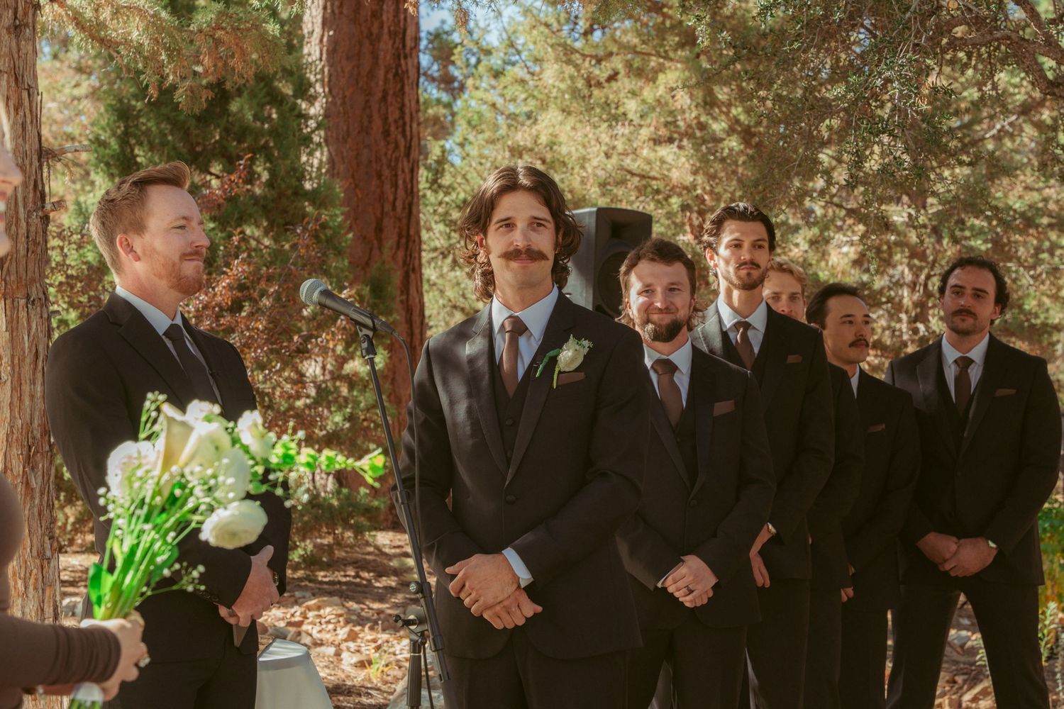 Groomsmen gather for a casual moment during an outdoor forest wedding.