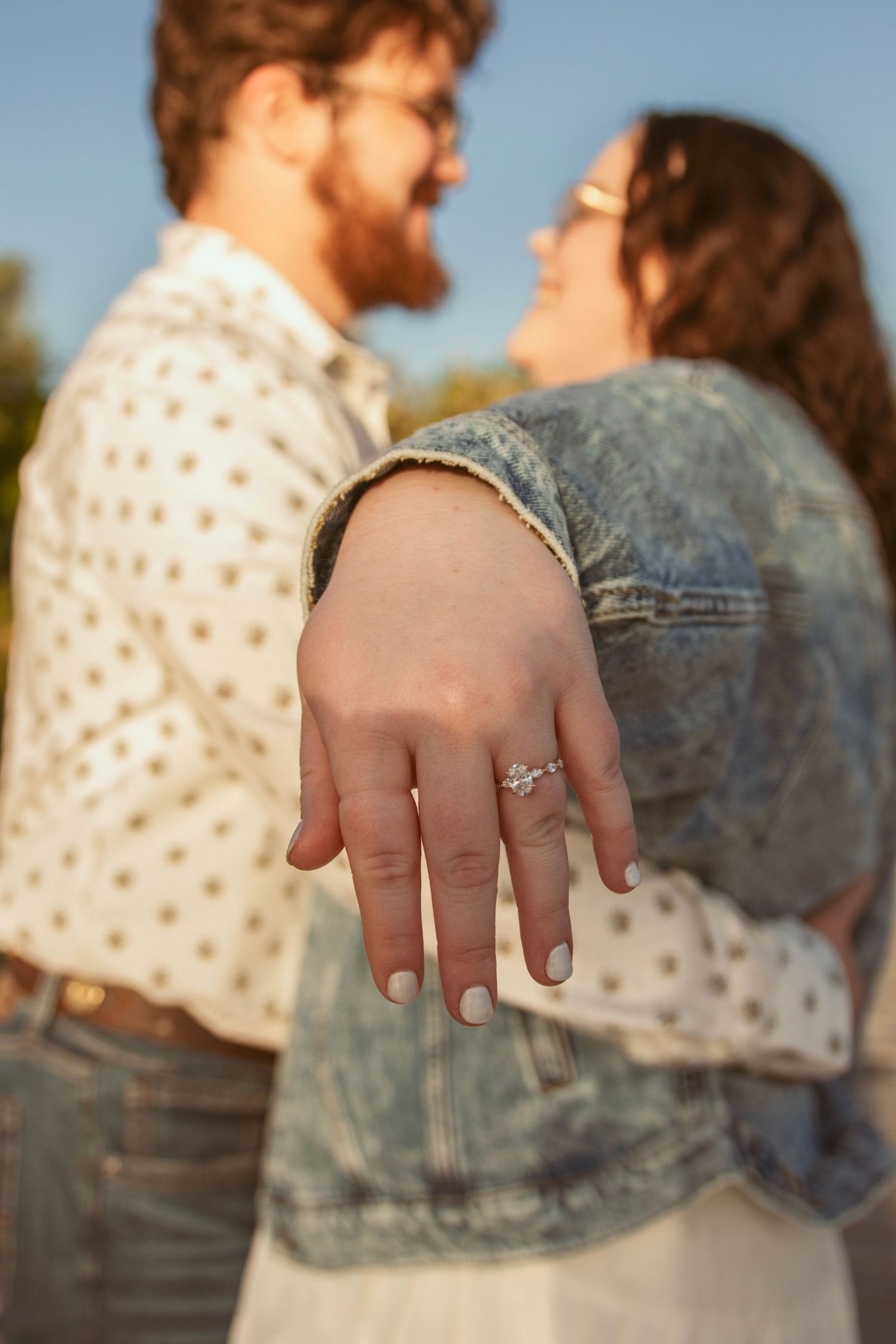 Close-up of hands showing off a sparkling engagement ring in golden sunlight.