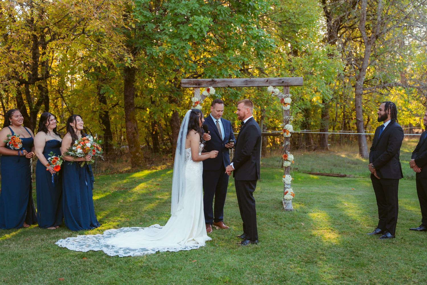Wedding ceremony taking place on grass lawn with autumn trees creating natural backdrop.