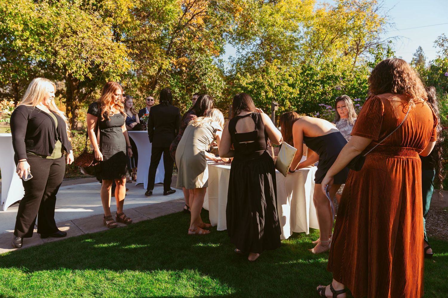 Wedding guests gathered outdoors under autumn trees during a daytime celebration.