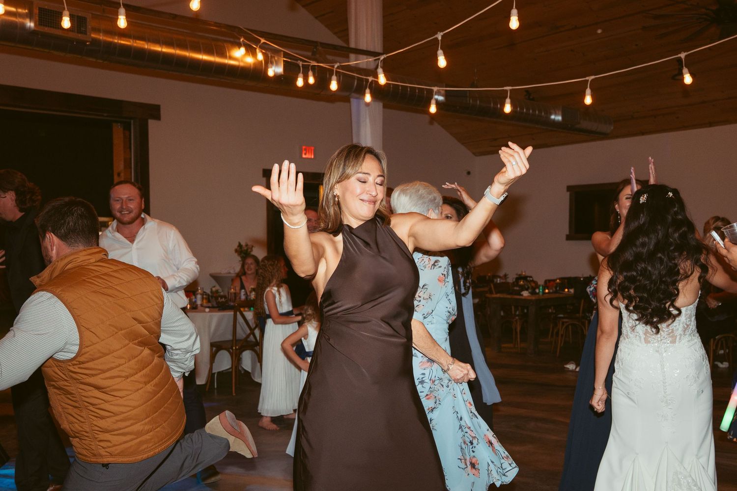 People dancing and celebrating at a wedding reception under warm string lights.