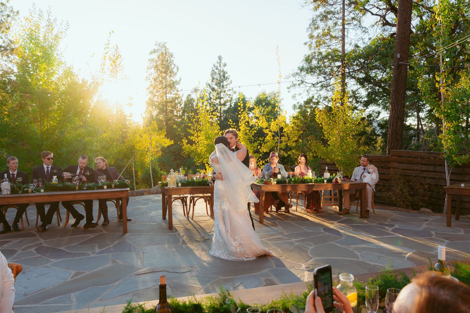 Wedding celebration on outdoor patio with golden sunset light streaming through the trees.
