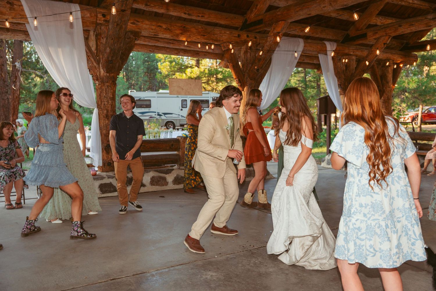 Wedding celebration with guests dancing in a covered outdoor venue with string lights overhead.