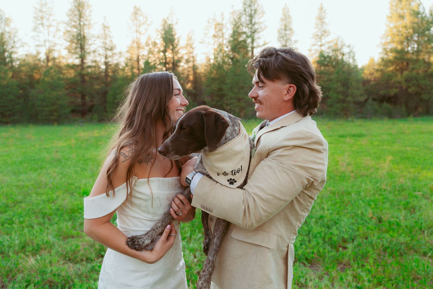 A couple shares tender moments with their dog in an outdoor field during golden hour.