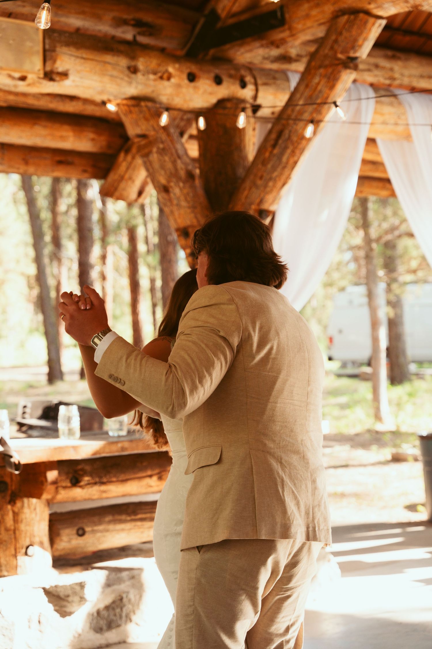 Couple sharing an intimate dance moment in a sunlit rustic pavilion.
