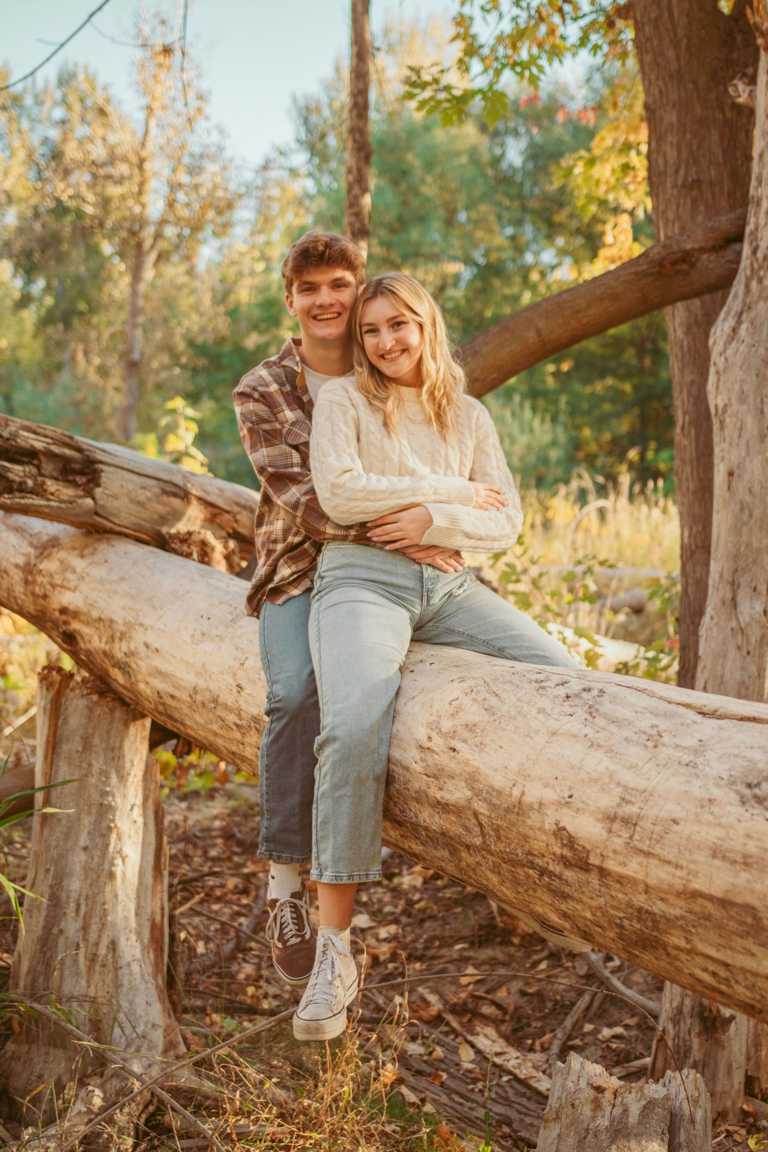 A couple poses together on a fallen tree trunk in an autumn setting.