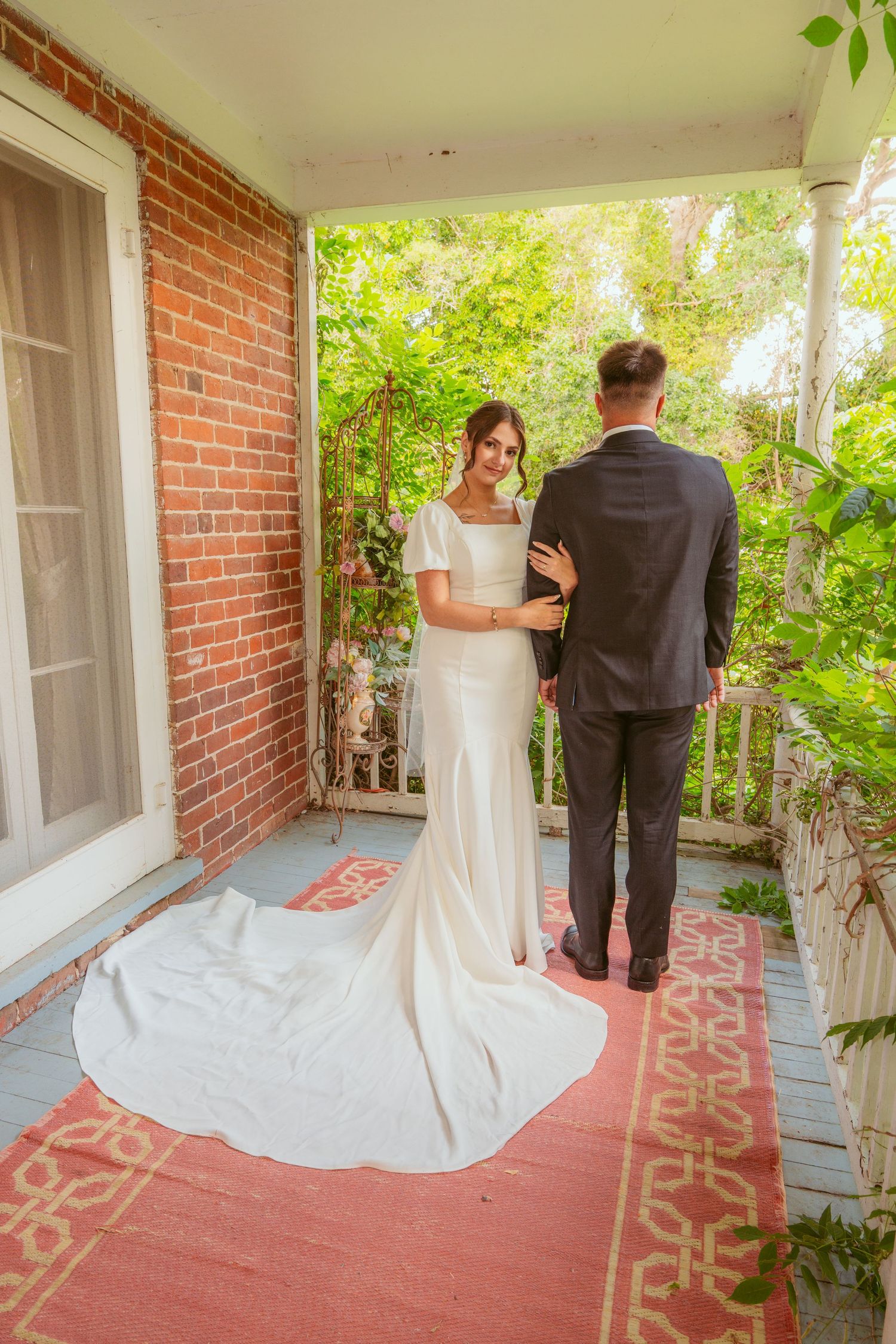A wedding couple stands on a brick porch with decorative floor tiles.