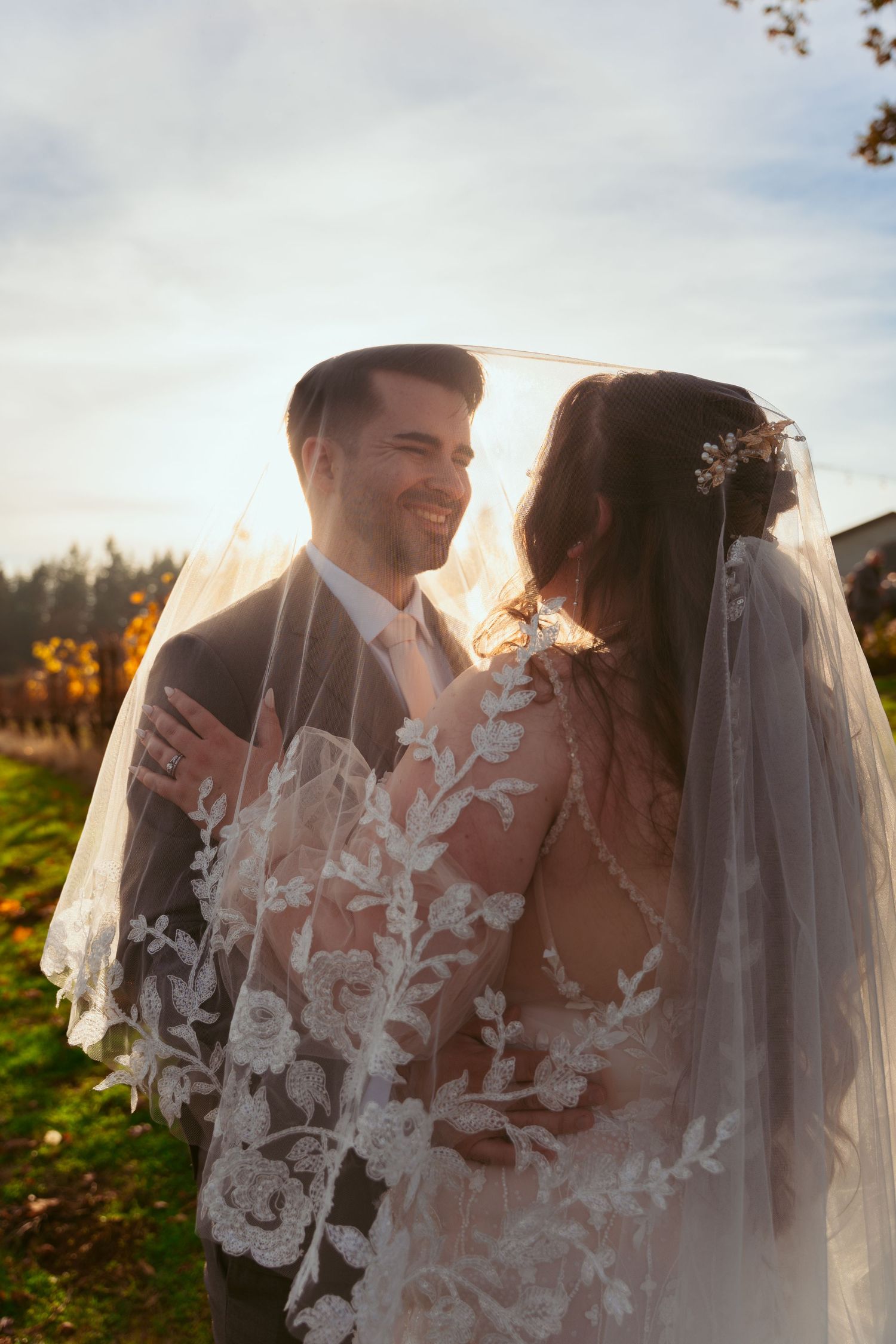 Sunlit wedding portrait with couple sharing an intimate moment under an ornate lace veil.