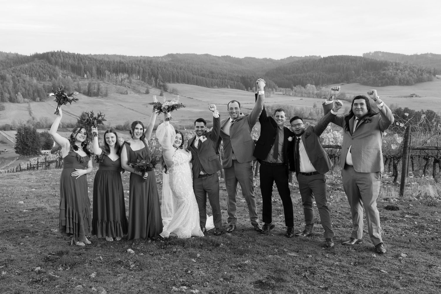 Wedding group stands in a line against rolling hills and mountains on an autumn day.