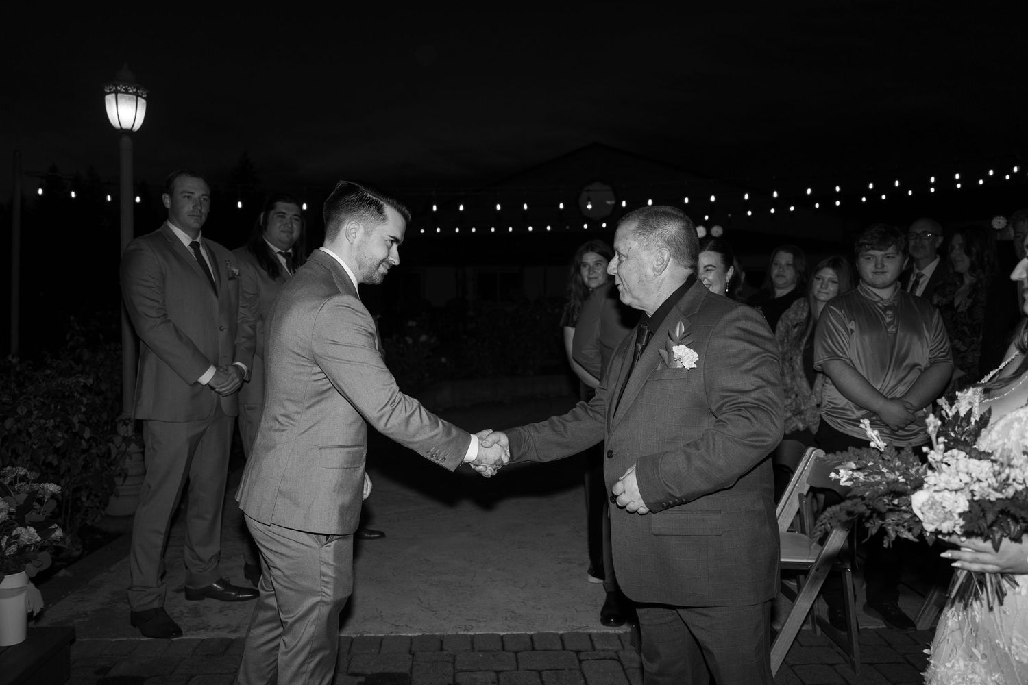 Wedding guests dancing and celebrating on an outdoor patio under string lights at night.