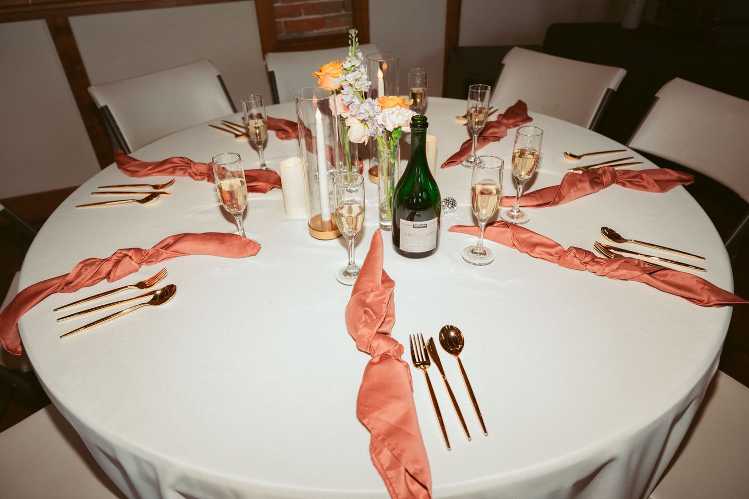 Round wedding reception table set with coral napkins and champagne glasses.