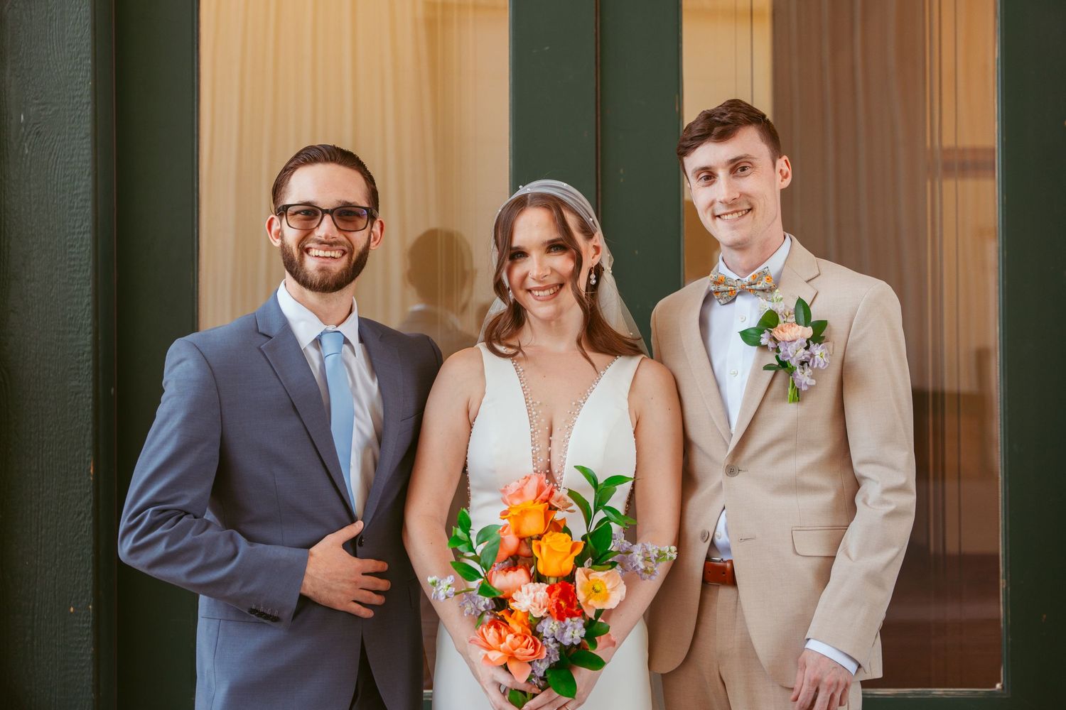 Wedding party members stand in formal attire with brown suits and light dresses.