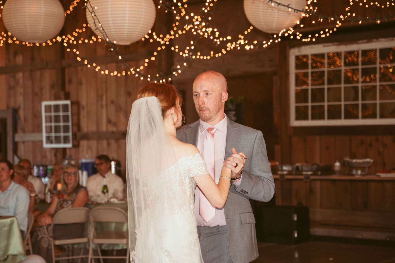Wedding reception in a rustic wooden barn adorned with fairy lights and white paper lanterns.