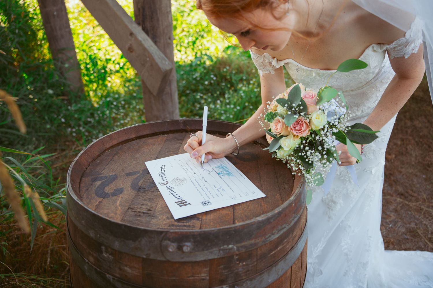 Newlyweds completing paperwork on vintage barrel during garden wedding ceremony.