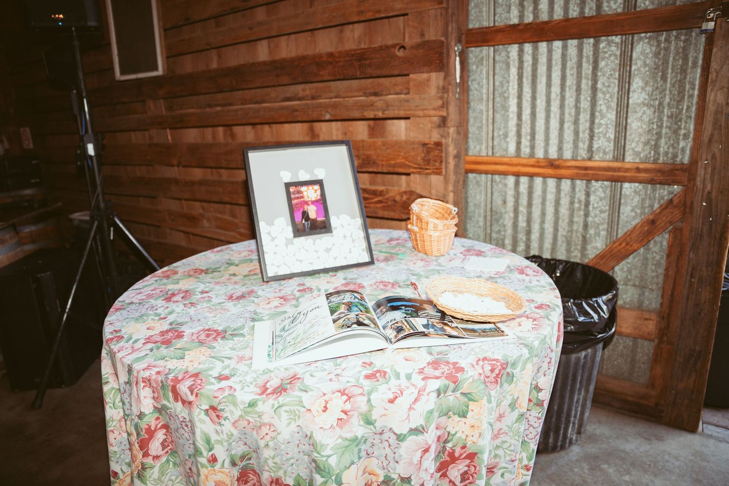 A small table with floral tablecloth displays a framed photo and decorative items in a rustic wooden room.