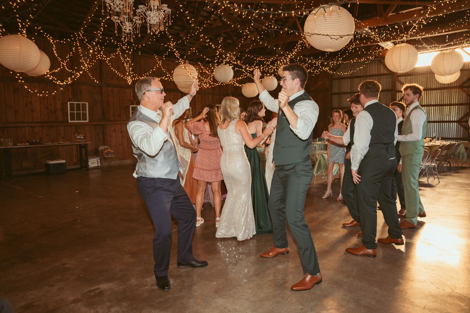 Couples dance together during a wedding reception under romantic string lights and paper lanterns.