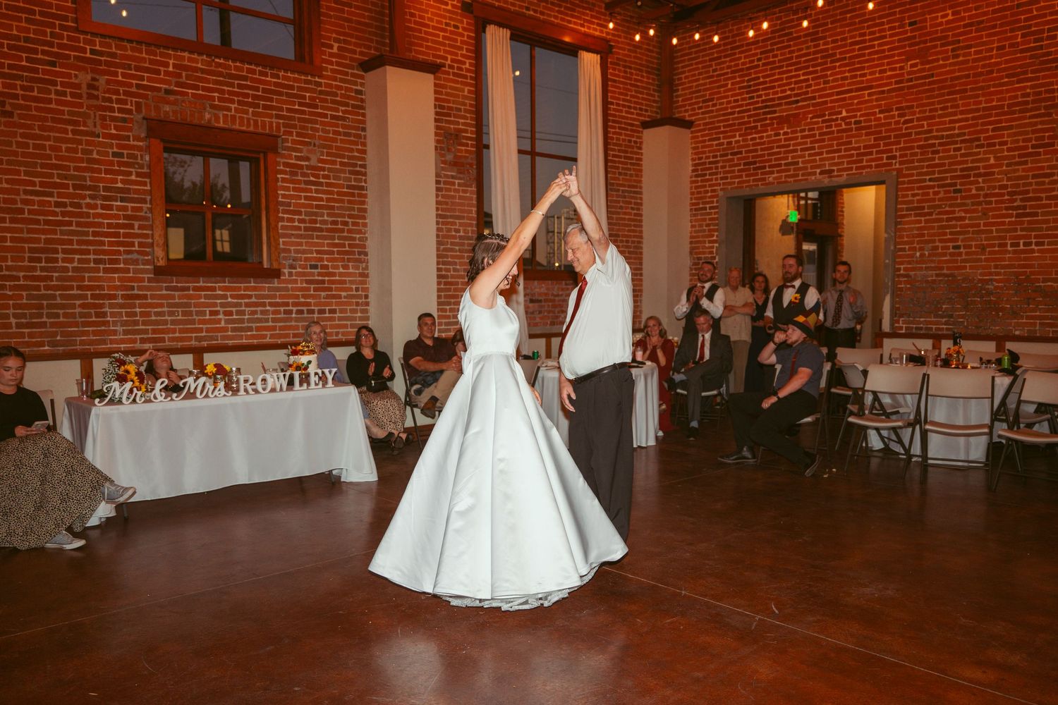 Wedding reception dance floor scene with string lights and exposed brick walls.