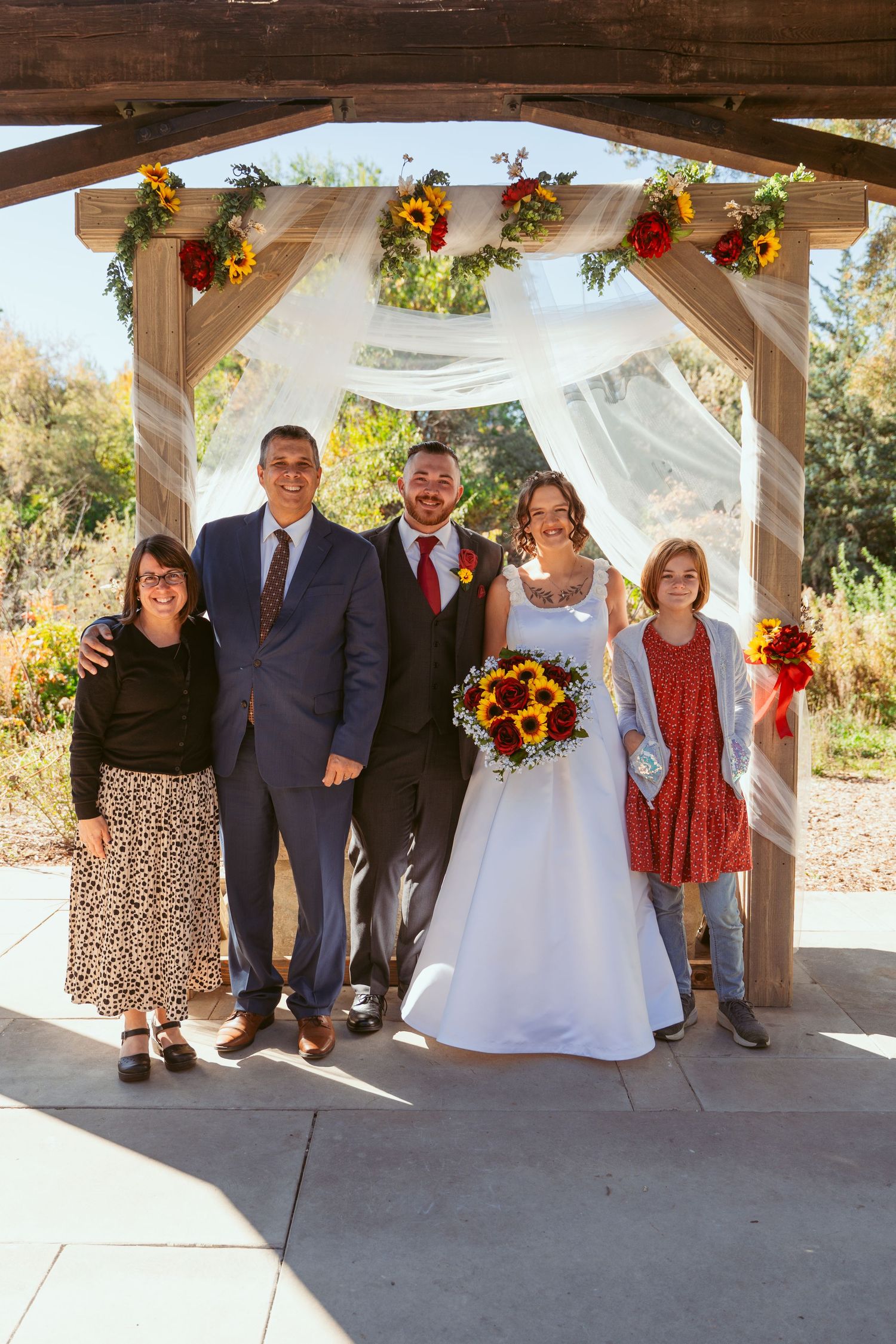 Wedding group photo session under wooden pavilion with sunflower decorations and white drapery.