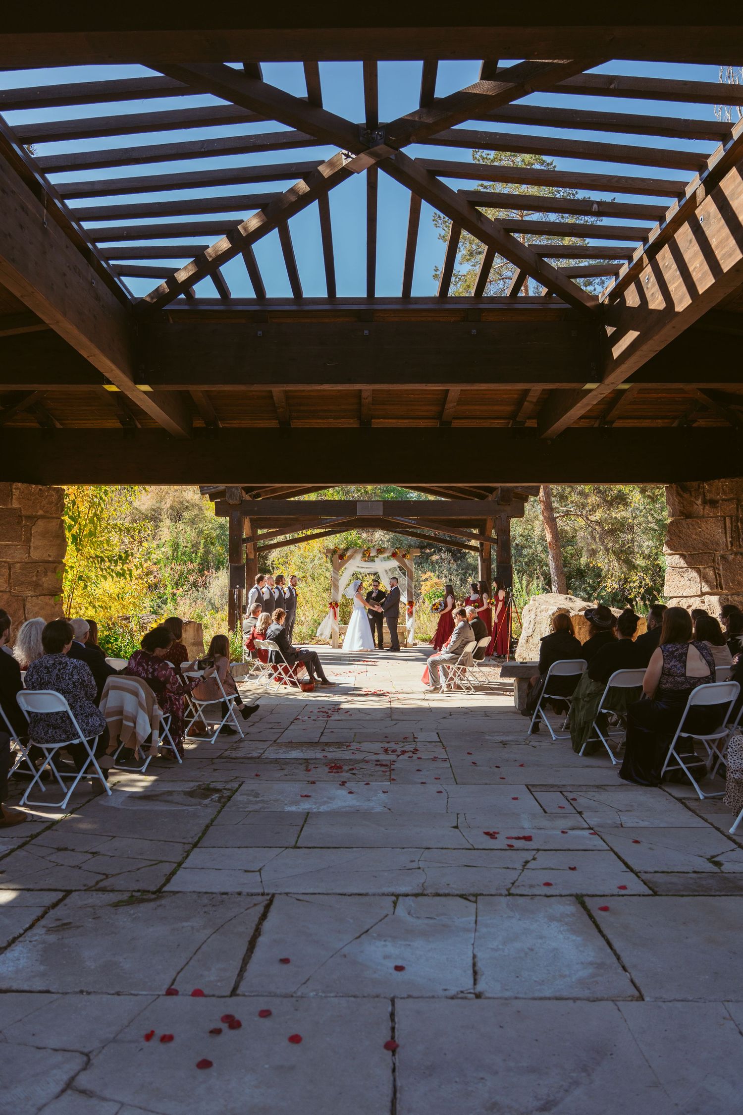 Empty wedding venue with wooden pergola and stone columns under blue sky.