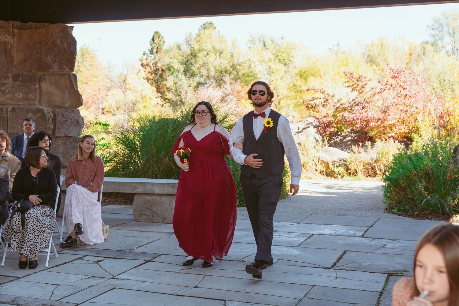 People mingle on a stone patio during an outdoor event with fall colors in the background.