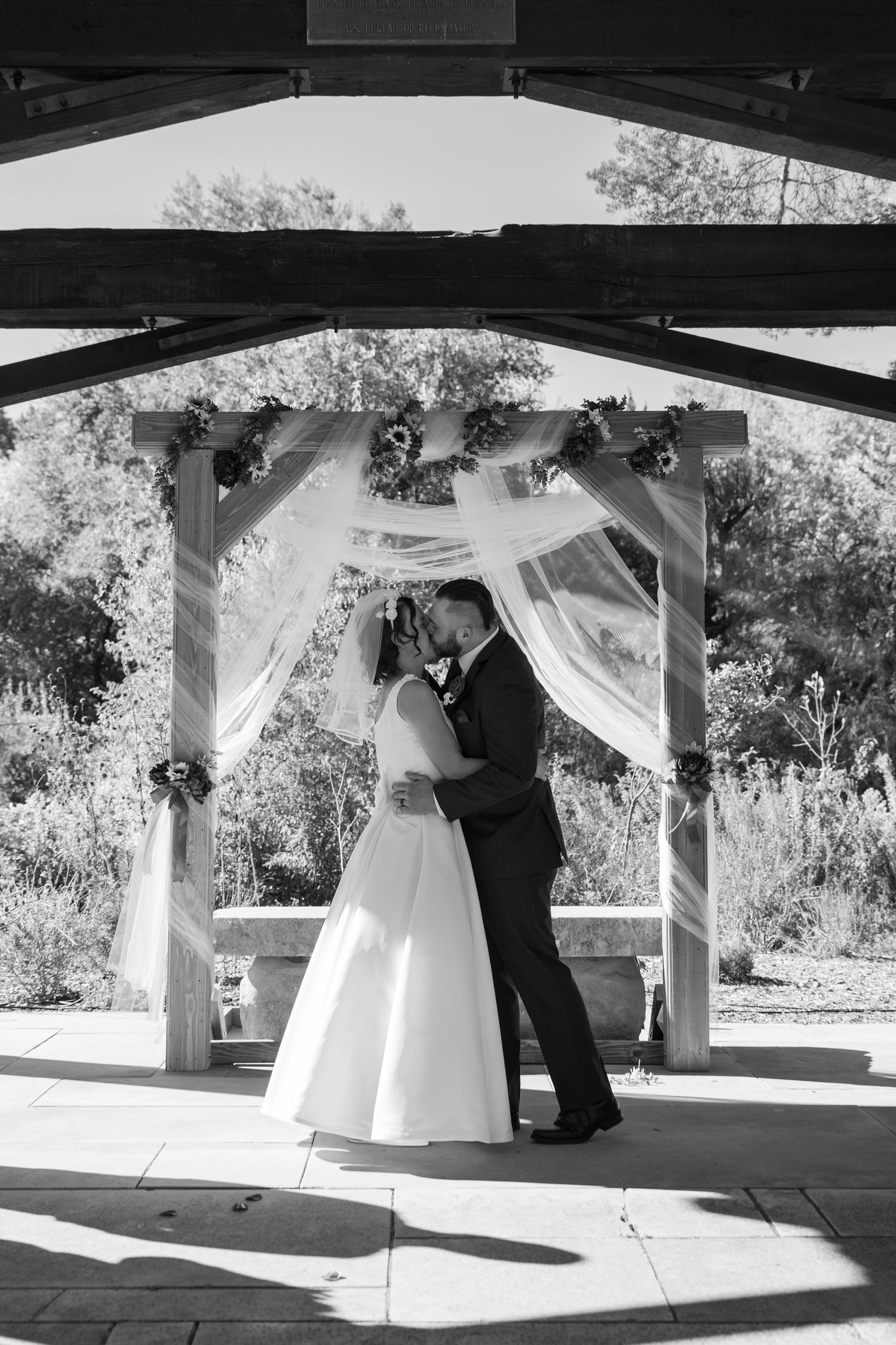 A wedding ceremony taking place under a rustic wooden pavilion with dramatic lighting and shadows.