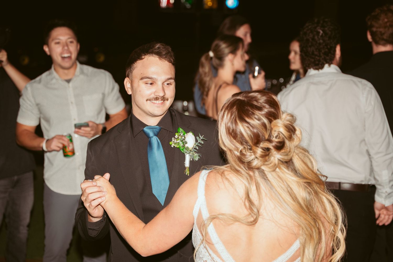 Guests dancing together at a wedding reception with string lights visible in the background.