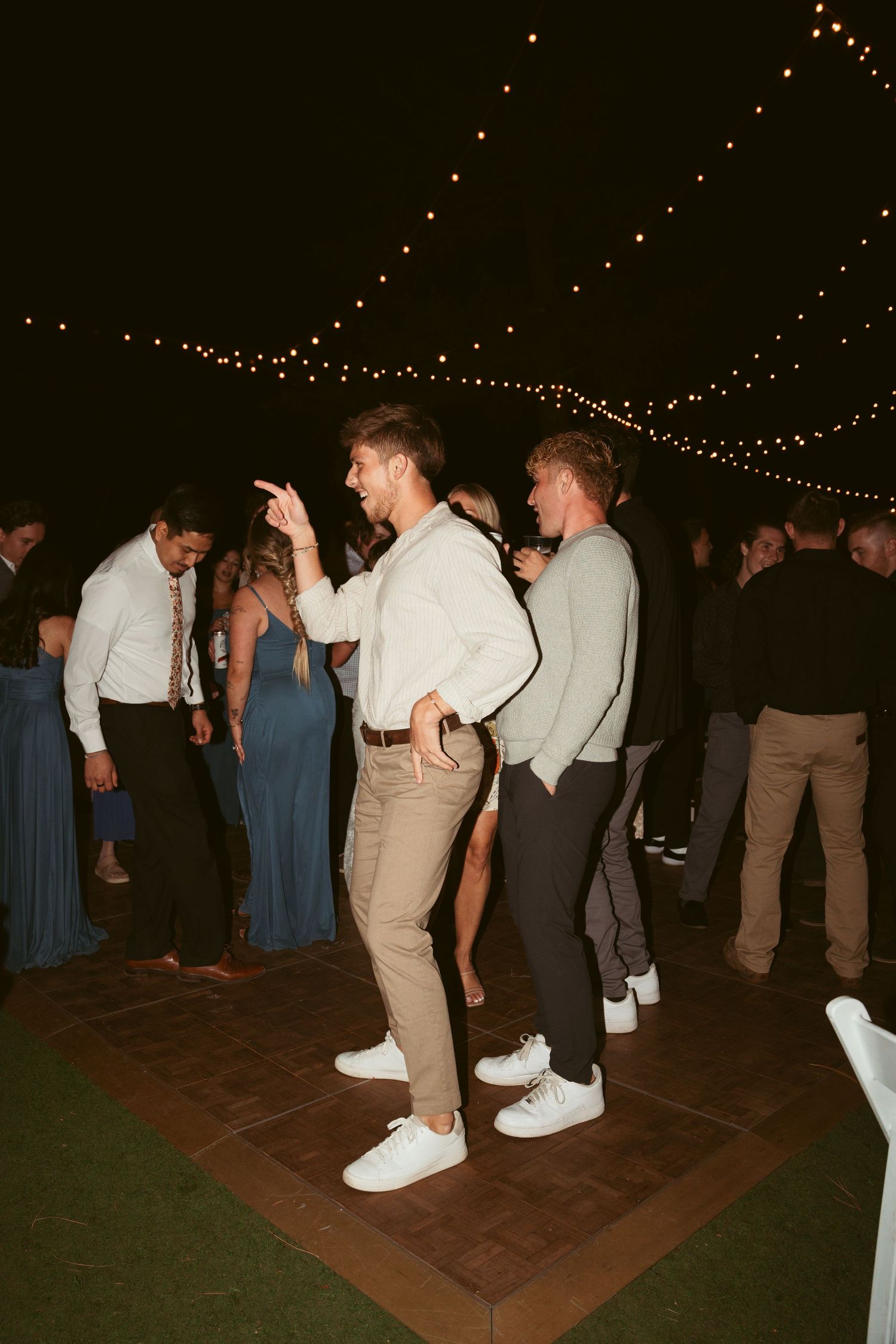 Partygoers dancing on a wooden floor beneath twinkling lights at a festive evening event.