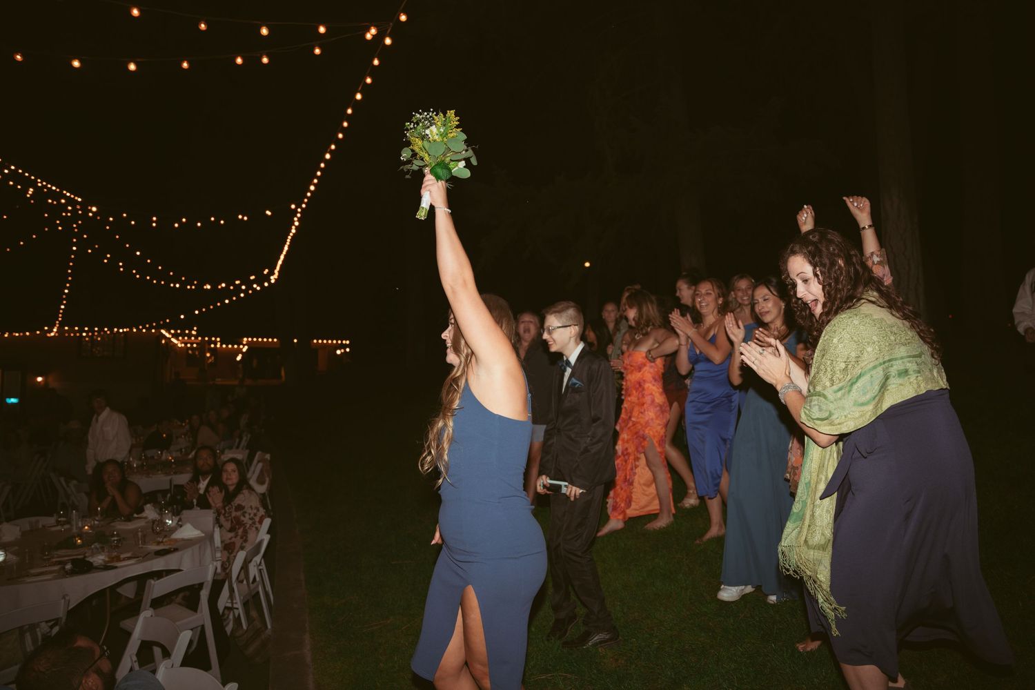 Wedding guests dance and celebrate on an outdoor dance floor under string lights at night.