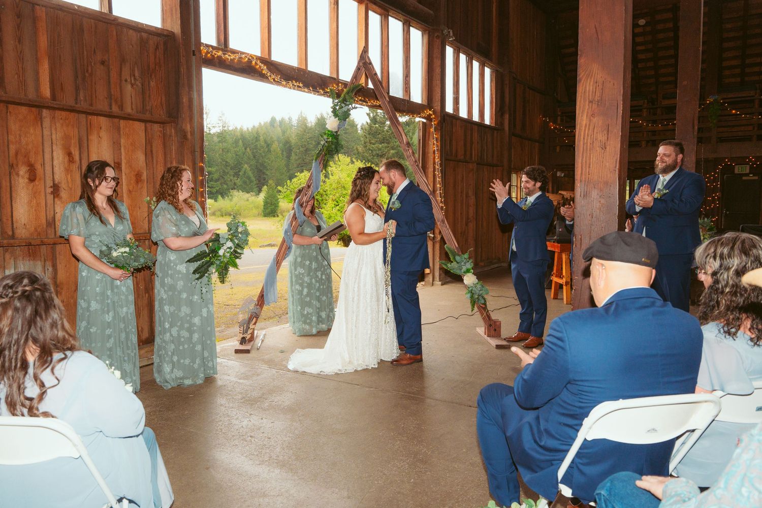 Wedding celebration in progress inside a spacious wooden barn with high ceilings and natural lighting.