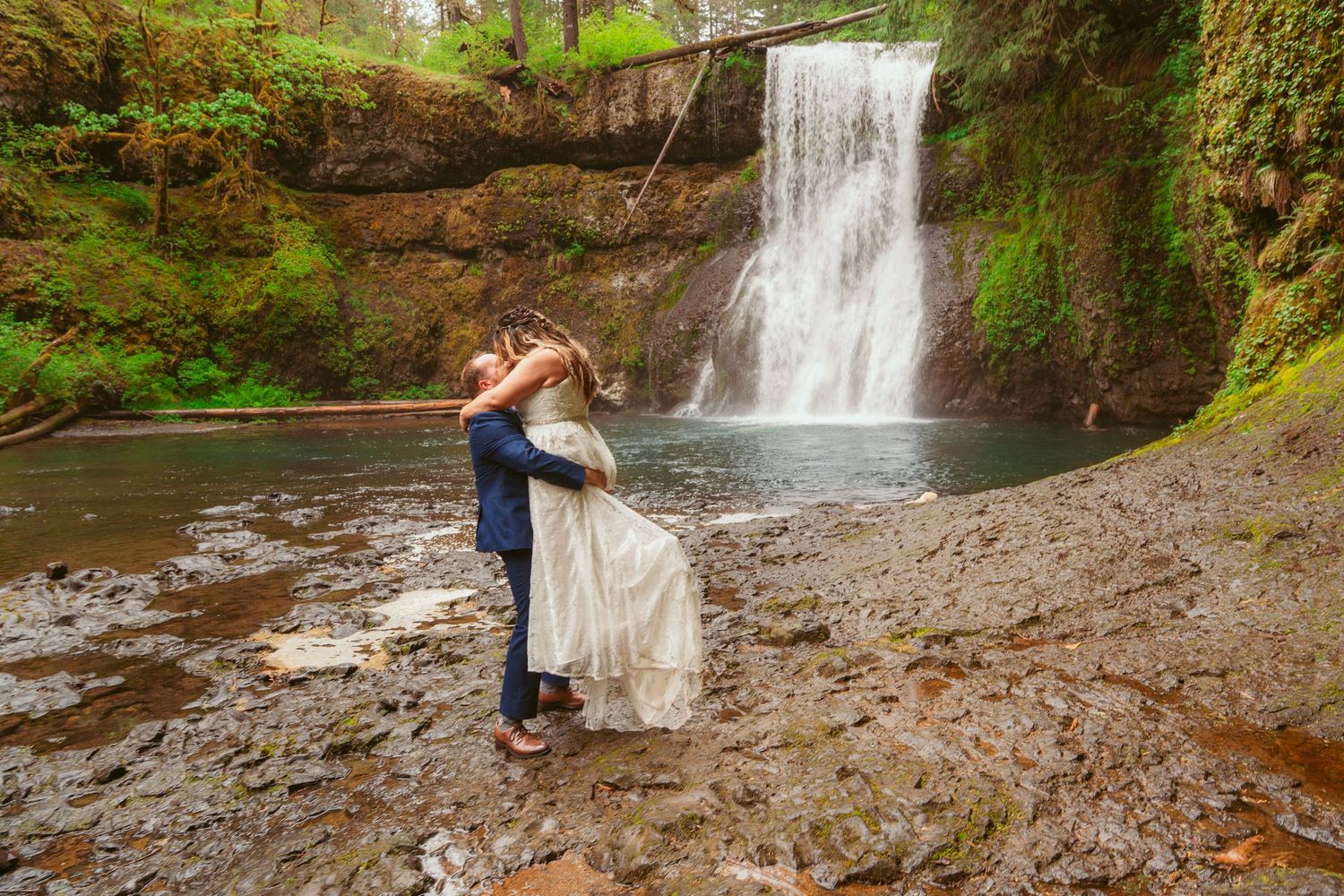 A romantic embrace by a cascading waterfall during a wedding photoshoot.