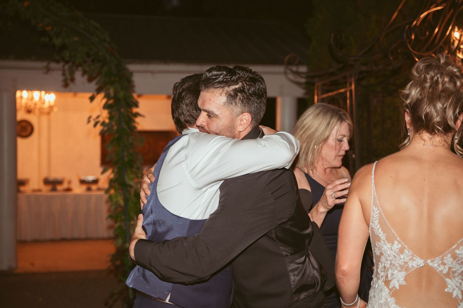 Couples slow dancing under warm lighting at an evening wedding reception.