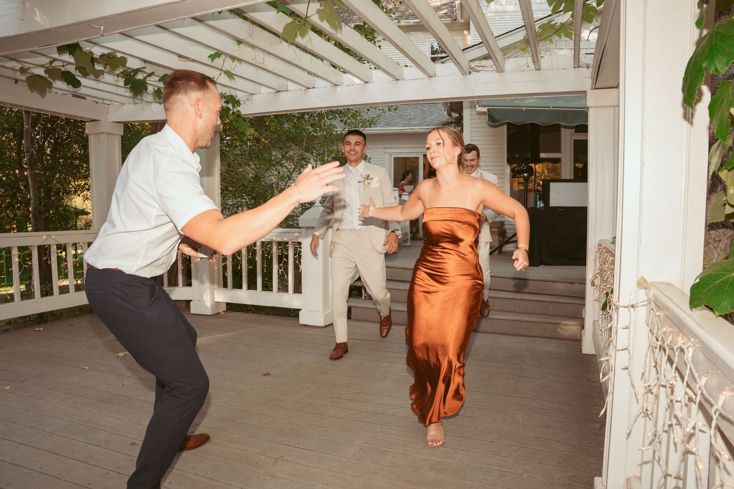 Wedding guests dance and celebrate on an outdoor porch decorated with greenery and white columns.