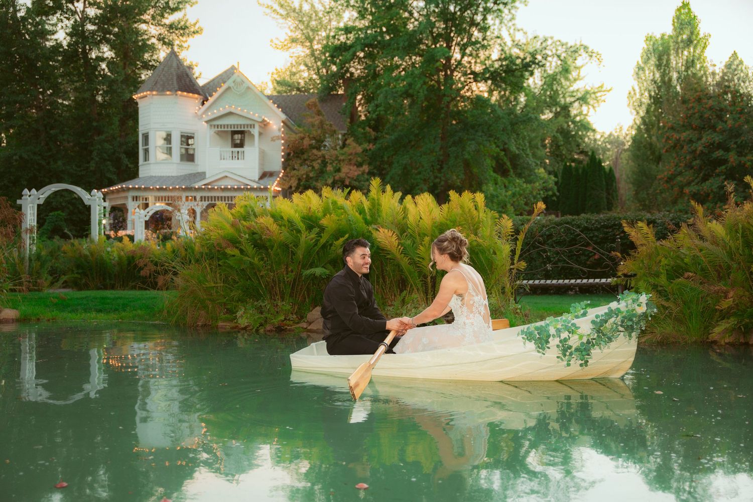 Wedding couple shares intimate moments in garden setting with Victorian architecture.