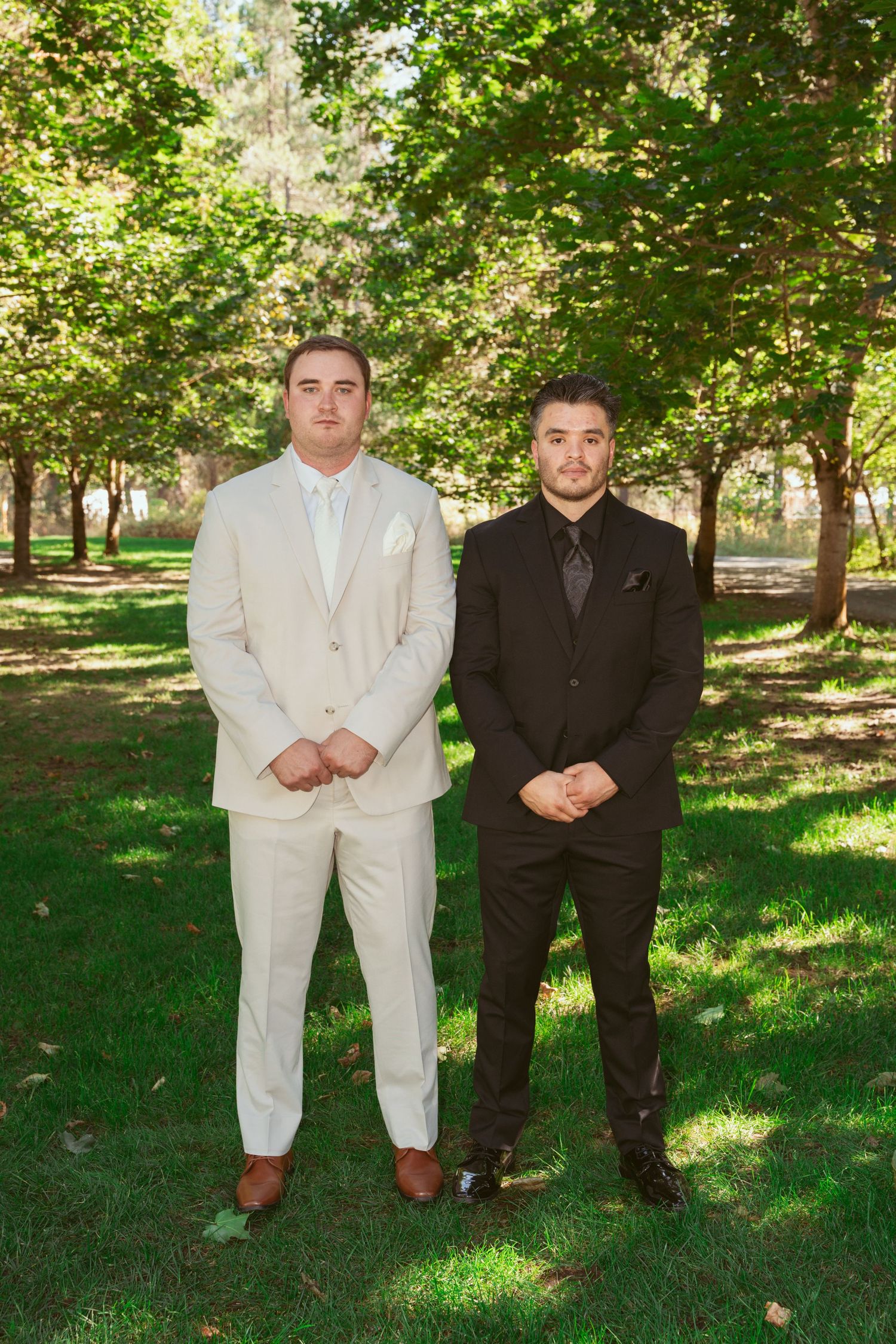 Groomsmen in contrasting black and white suits pose on grass under trees.