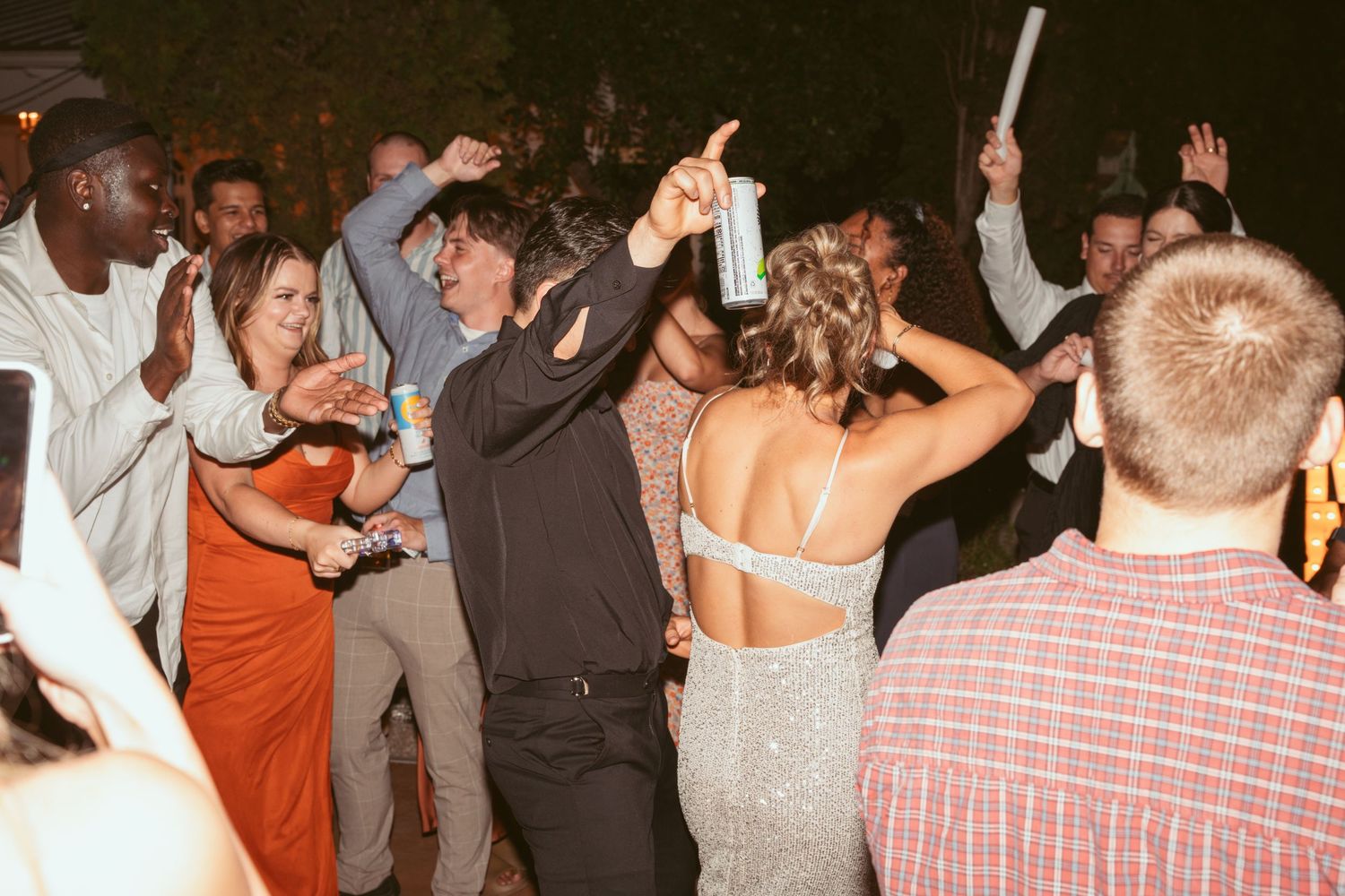 Wedding guests dancing and celebrating on a dance floor at night with drinks in hand.