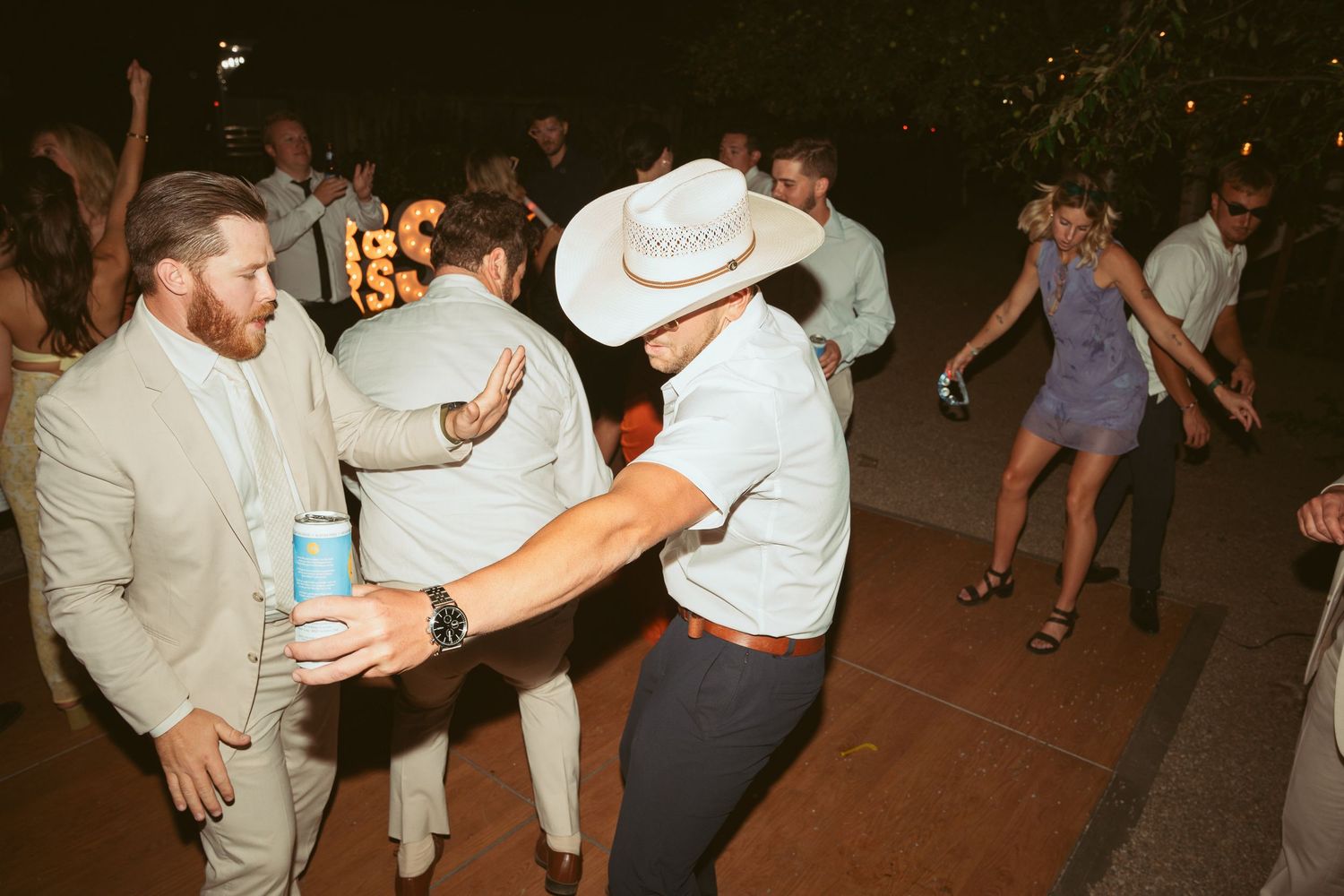 Wedding guests in cowboy hats dancing at outdoor reception party.