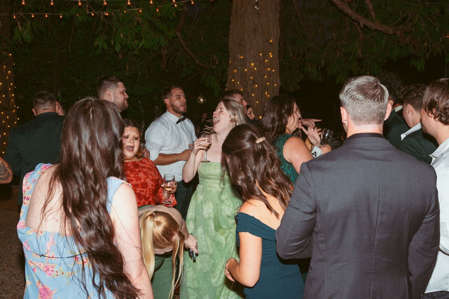 Wedding guests dance and celebrate on an outdoor dance floor decorated with string lights at night.