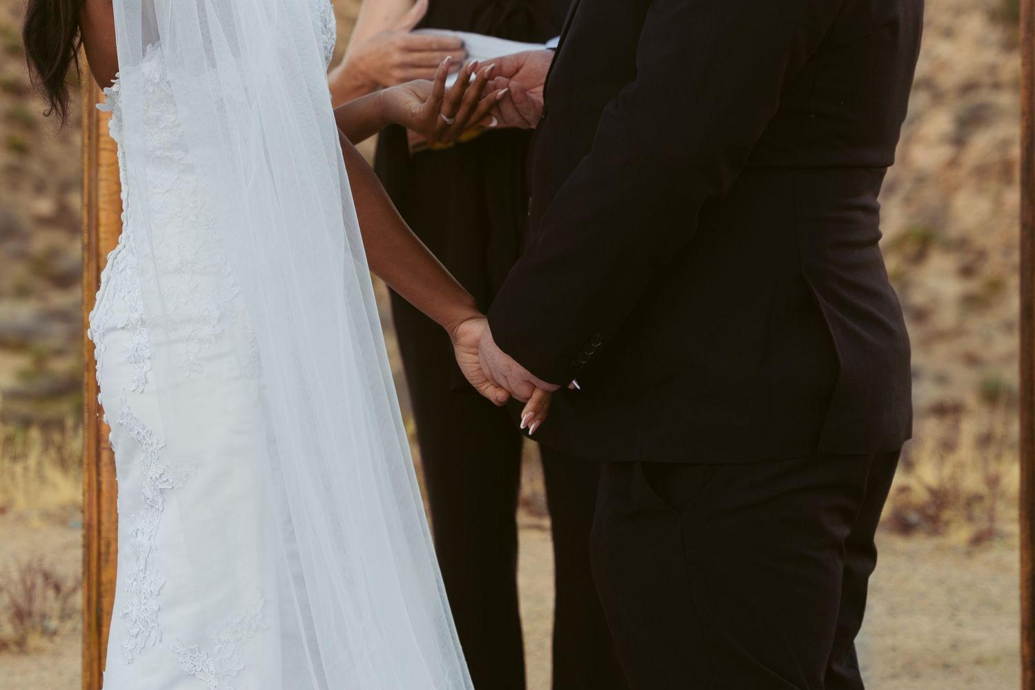 Close-up shot of wedding couple's hands during ceremony in outdoor desert setting.