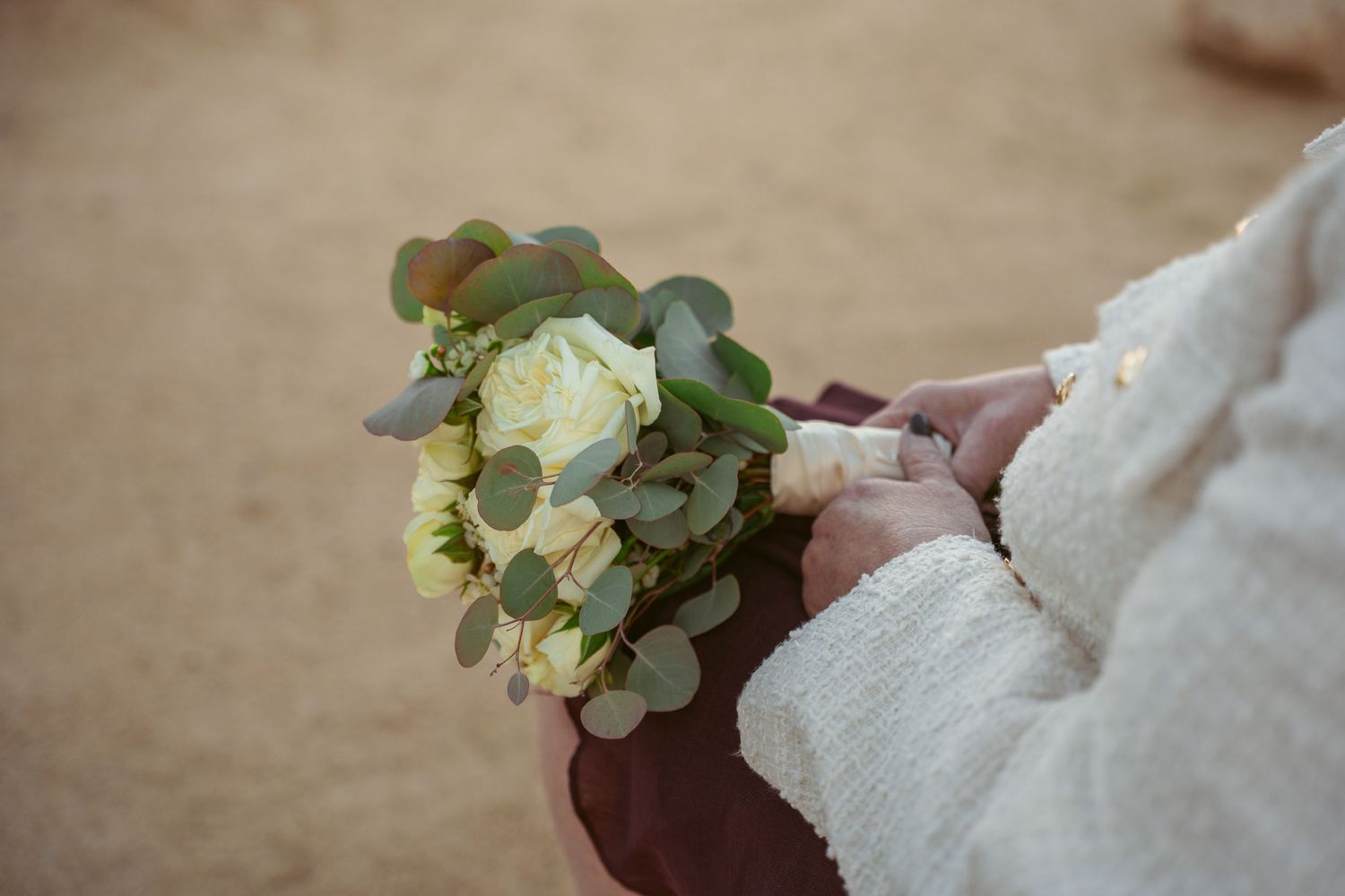 Close-up of a white and green bridal bouquet with roses and eucalyptus held in lace-covered hands.