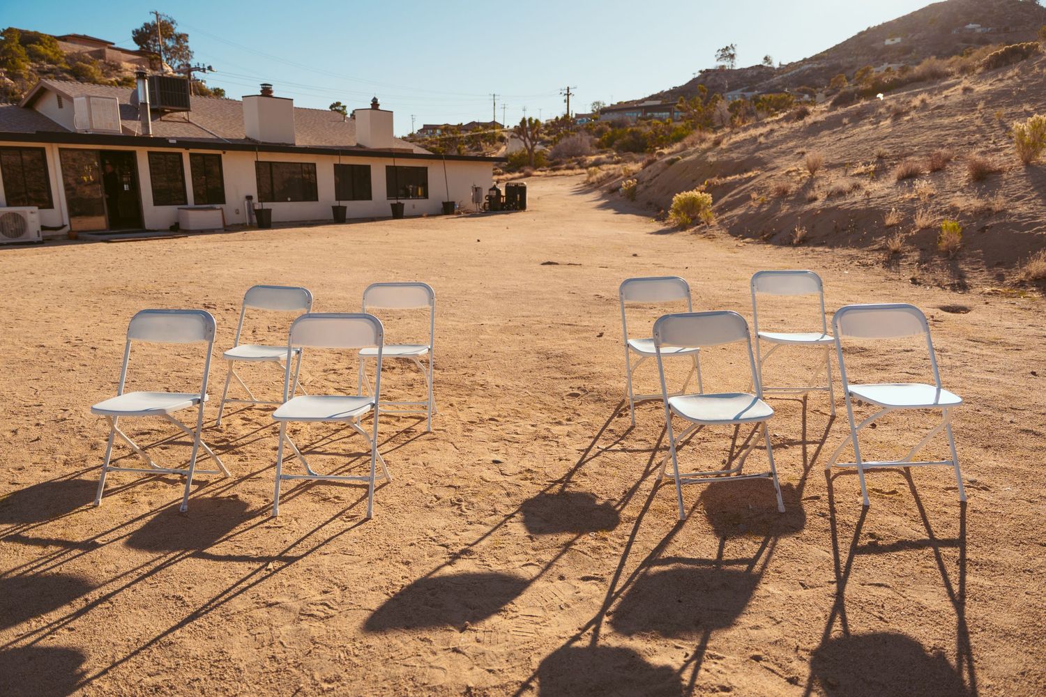 Metal chairs set up in rows on sandy desert terrain with mountains and blue sky.