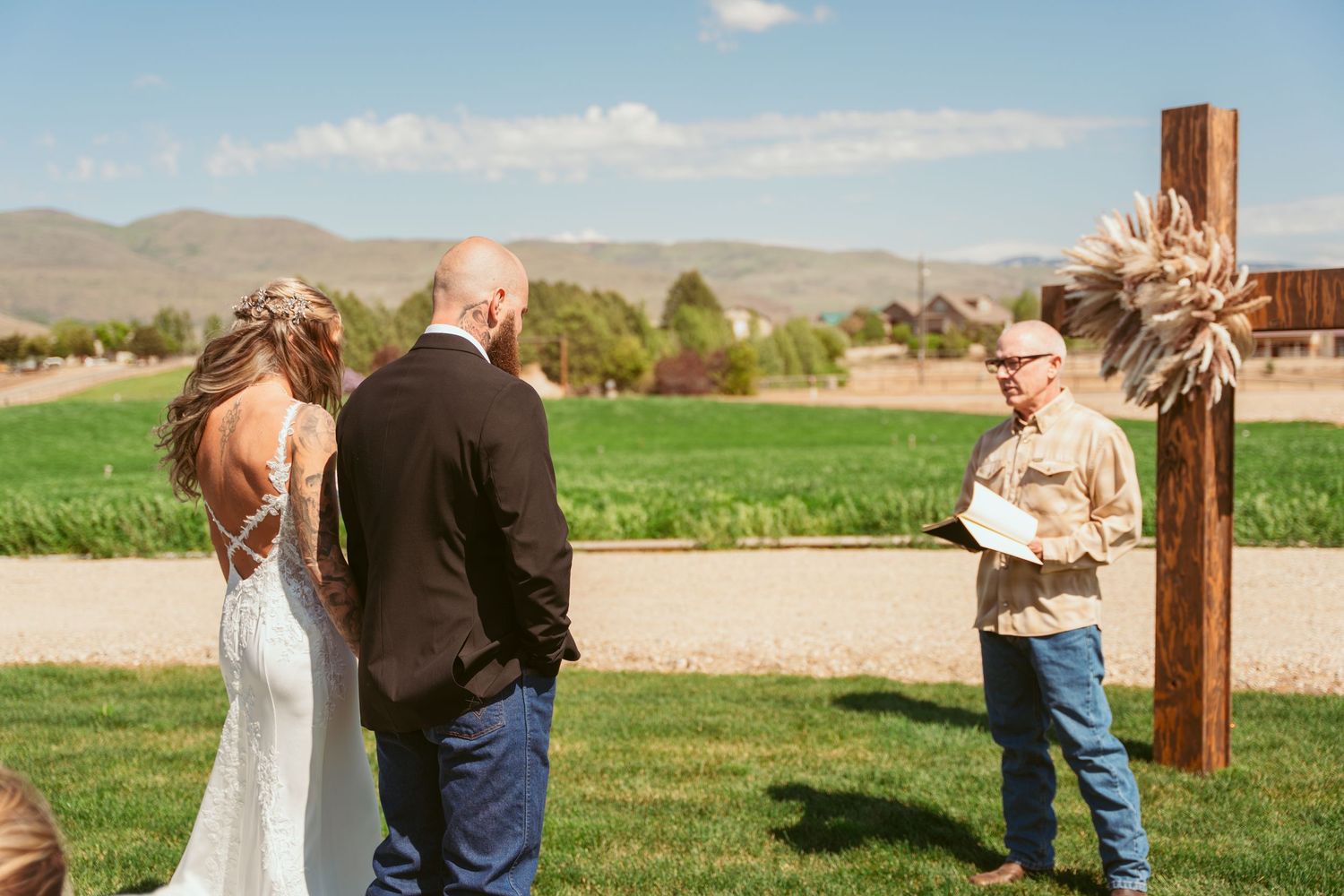 Outdoor wedding ceremony with wooden cross and white chairs against mountain landscape.