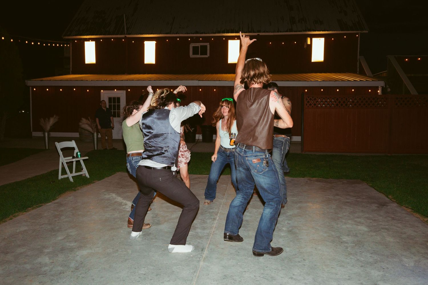 People dancing at an outdoor party venue with string lights overhead.