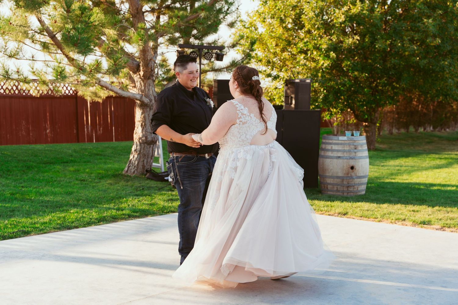 Wedding couple dancing outdoors on a paved area with trees and greenery in the background.