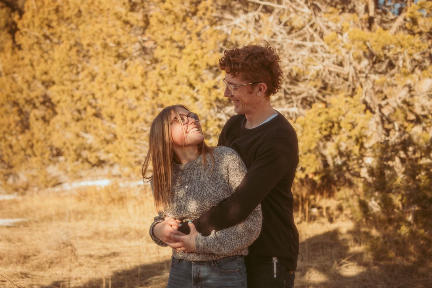 A couple embraces in front of golden autumn foliage during an outdoor photo session.