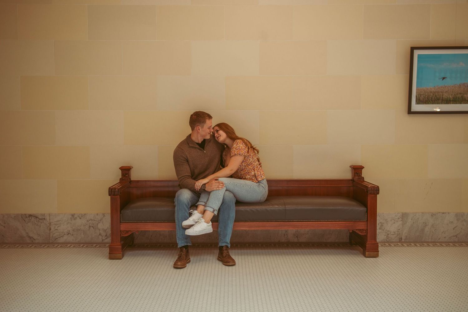 A couple shares romantic moments while sitting on wooden benches in an elegant hallway.