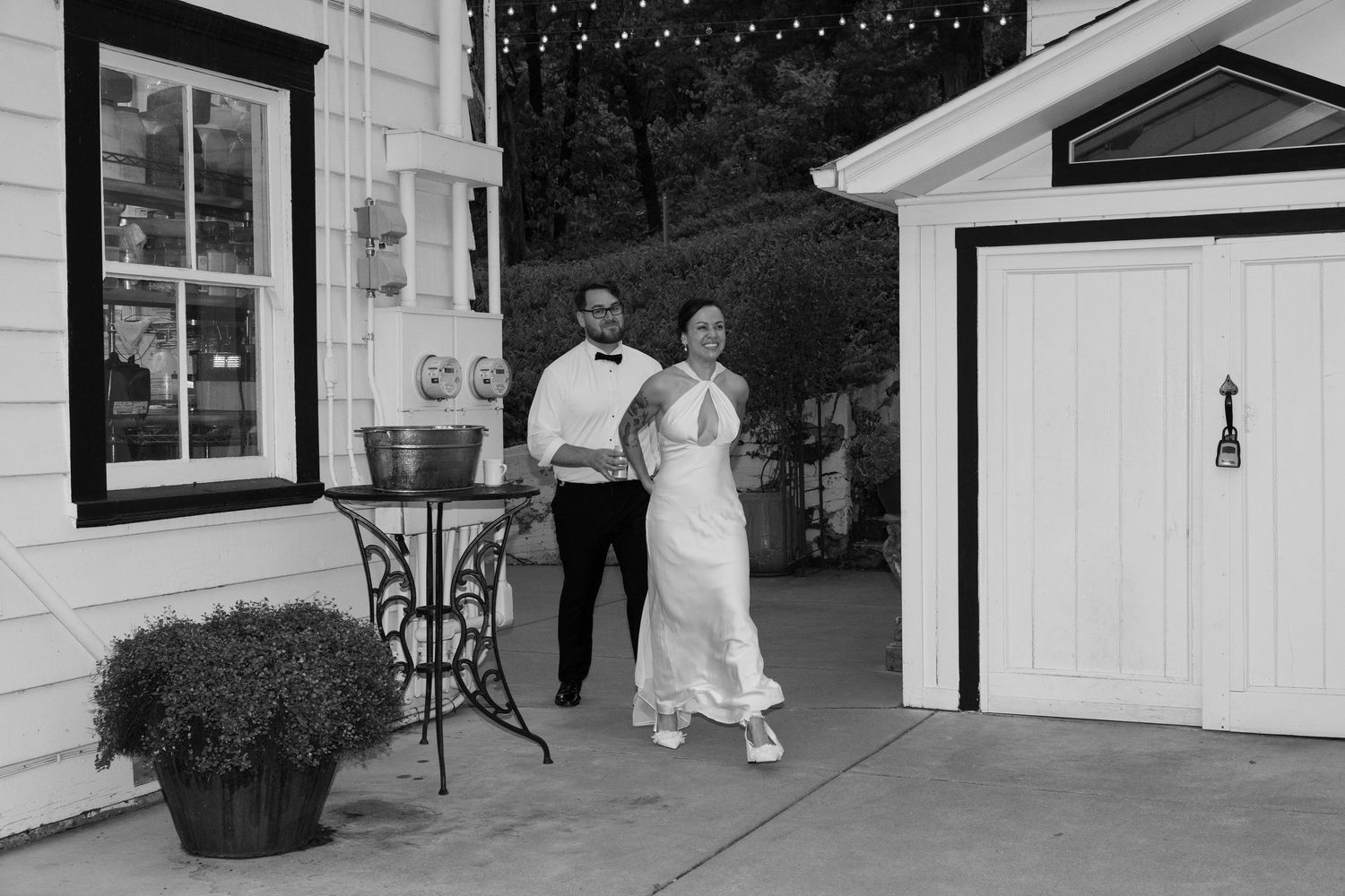 A couple walks together along a white building exterior in black and white.