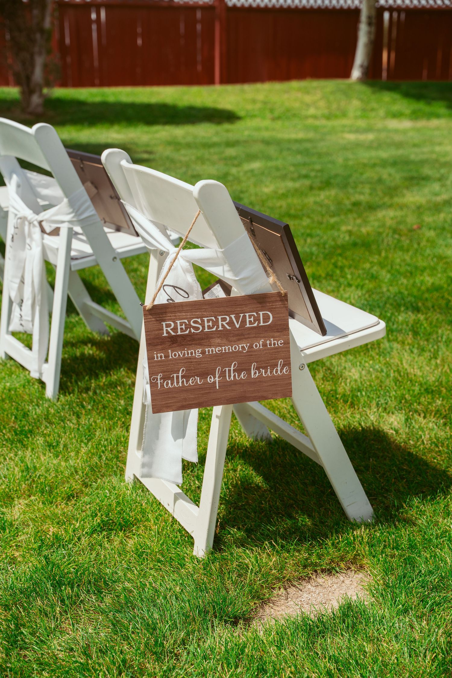Wooden reserved seating signs displayed on white folding chairs arranged on a green lawn for an outdoor wedding ceremony.