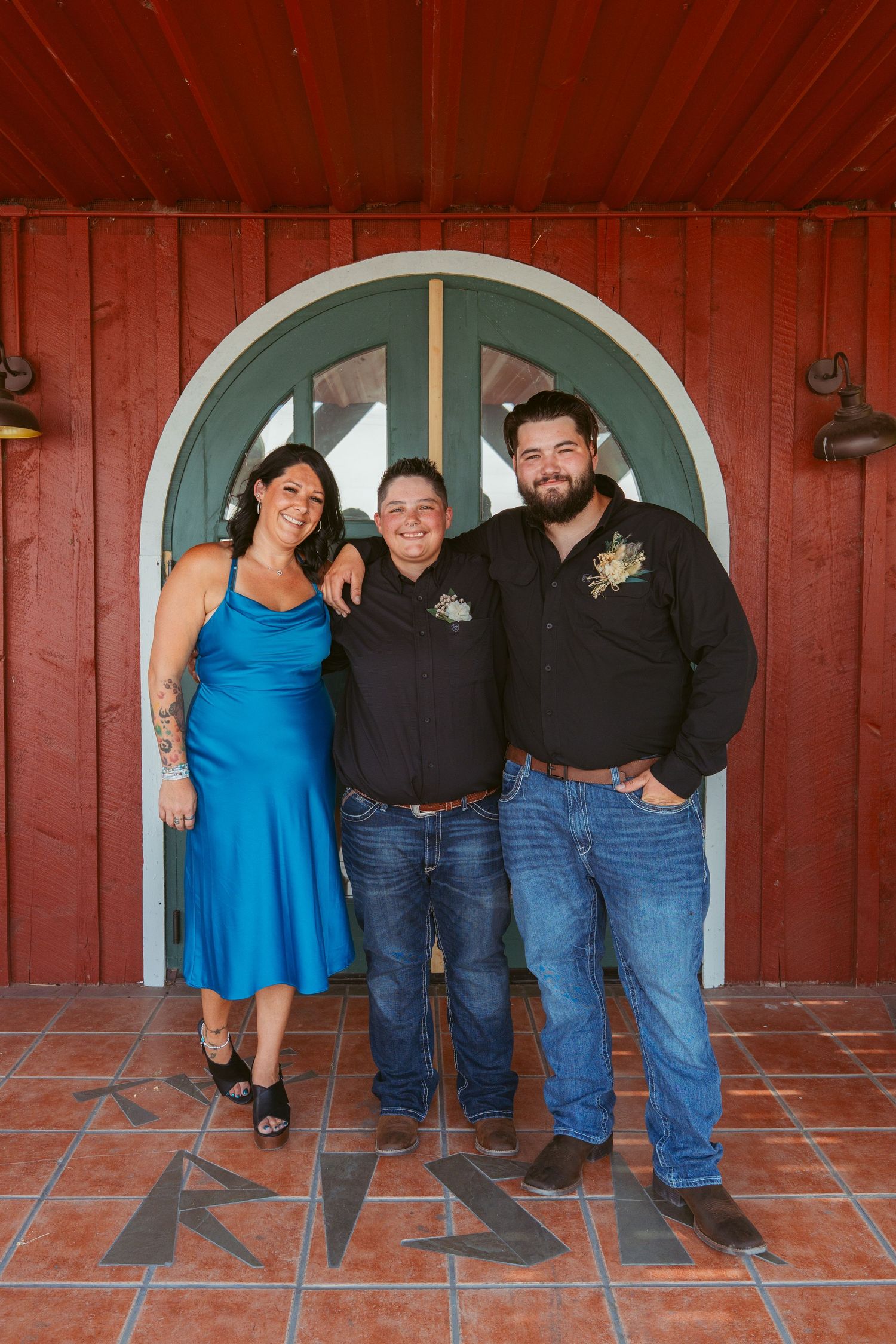 Three people pose together in front of red building, with one wearing bright blue dress.