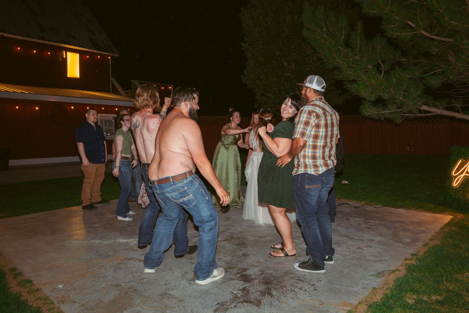 Wedding guests dancing and celebrating on an outdoor patio at night.